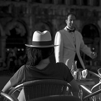 black and white photo on the St. Mark's Square at Caffè Florian a young lady sitting back with a clear cap shot by Claude Halet with a NIKON D3X